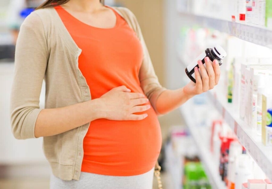 A pregnant woman holding a bottle of medication. Some women may wonder what to take if they have factor V Leiden while pregnant.