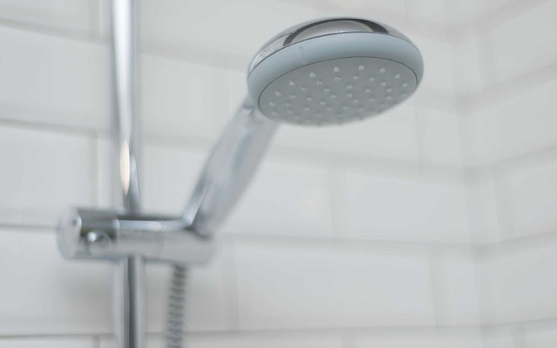 Close-up of chrome shower in the bathroom covered decorative ceramic tiles with white glossy bricks